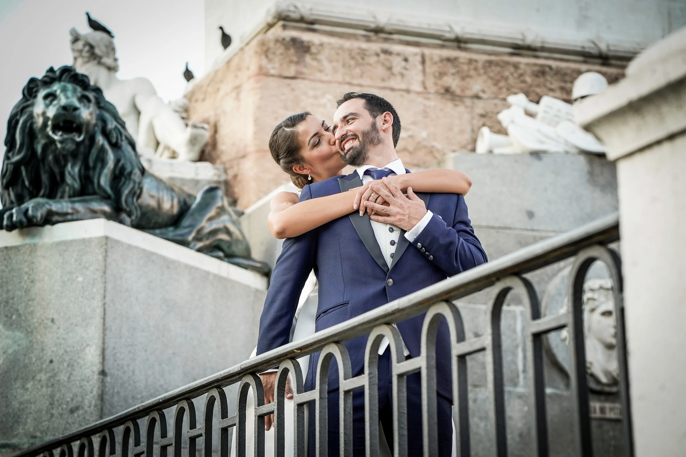Sara abraza a Edu junto a una escultura de león en el entorno del Palacio Real durante su postboda en Madrid.