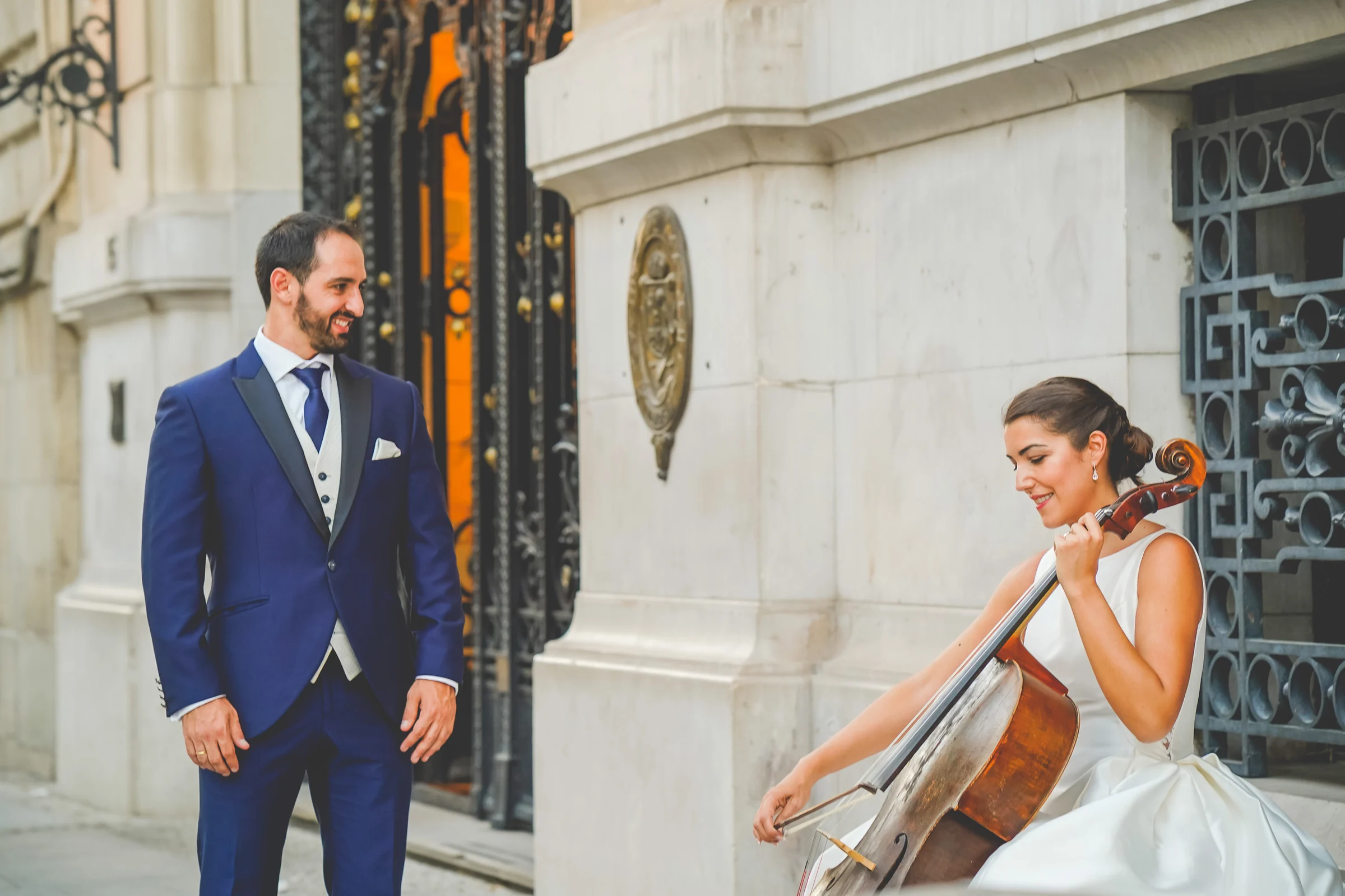Sara toca un violonchelo mientras Edu la observa durante una escena creativa de su postboda por el centro de Madrid.