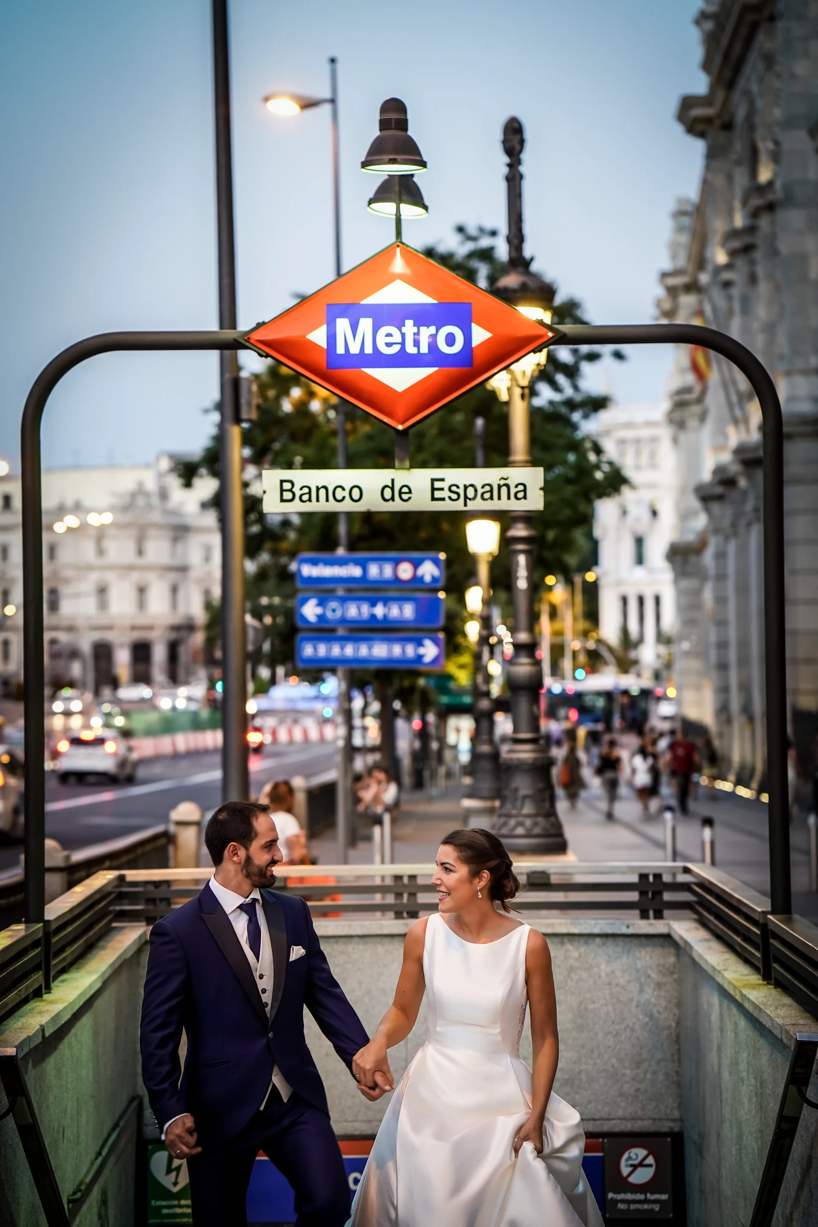 Sara y Edu suben de la mano por el acceso de Metro Banco de España durante su postboda por el centro de Madrid.