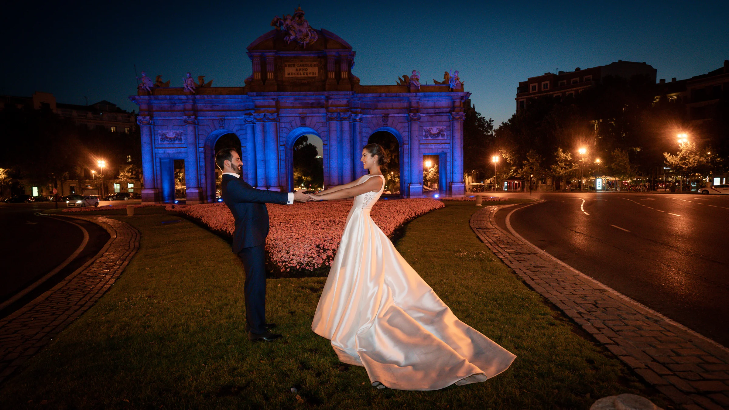 Sara y Edu giran frente a la Puerta de Alcalá iluminada durante la parte nocturna de su postboda en Madrid.