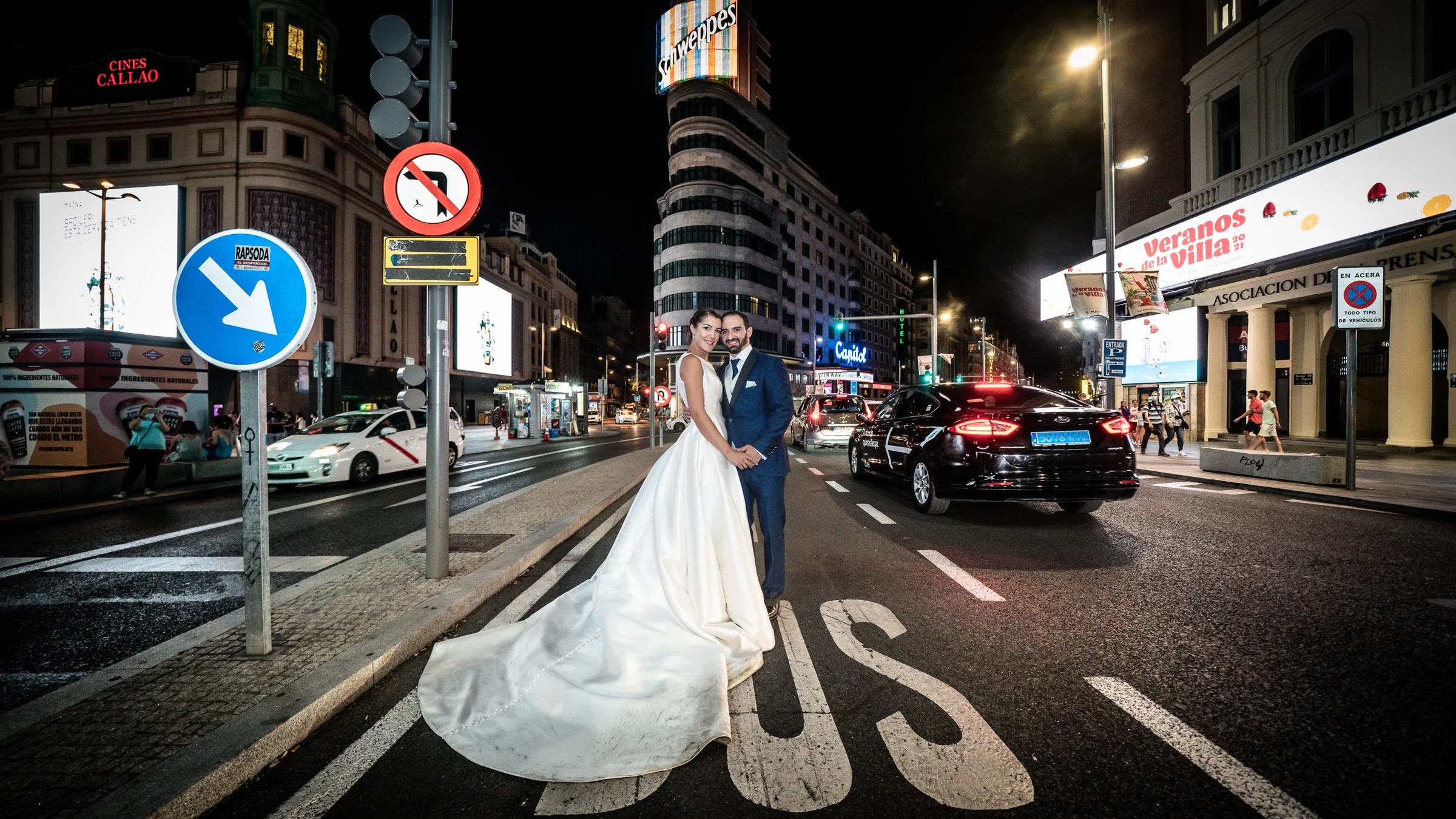 Sara y Edu posan en la calzada de Callao con los rótulos de Gran Vía iluminando su postboda nocturna en Madrid.