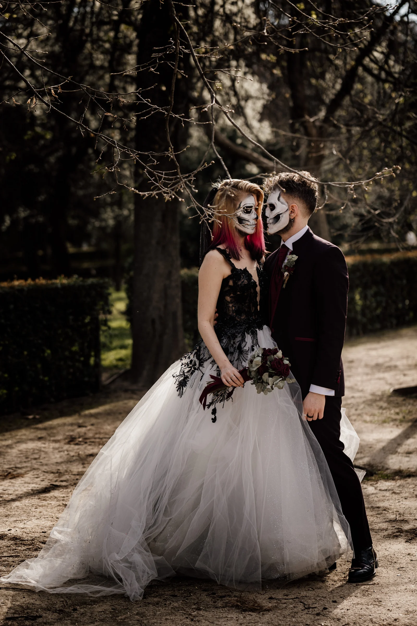 Silvia y Rubén se abrazan de pie entre los jardines de El Retiro mostrando su maquillaje de calavera durante la postboda.