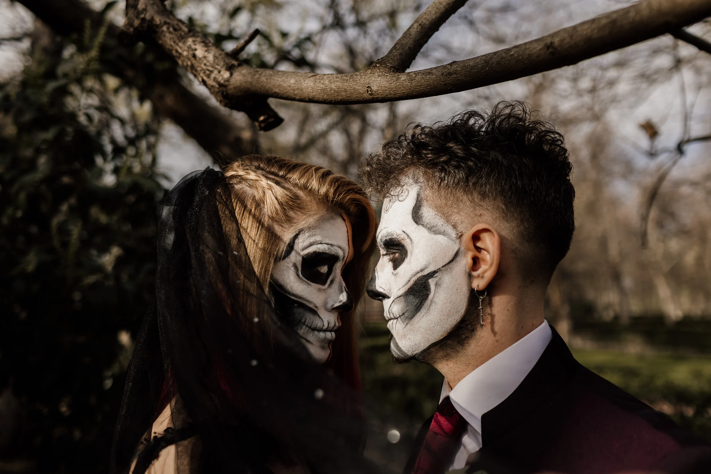 Primer plano de Silvia y Rubén acercando sus rostros con maquillaje de calavera entre los árboles de El Retiro.