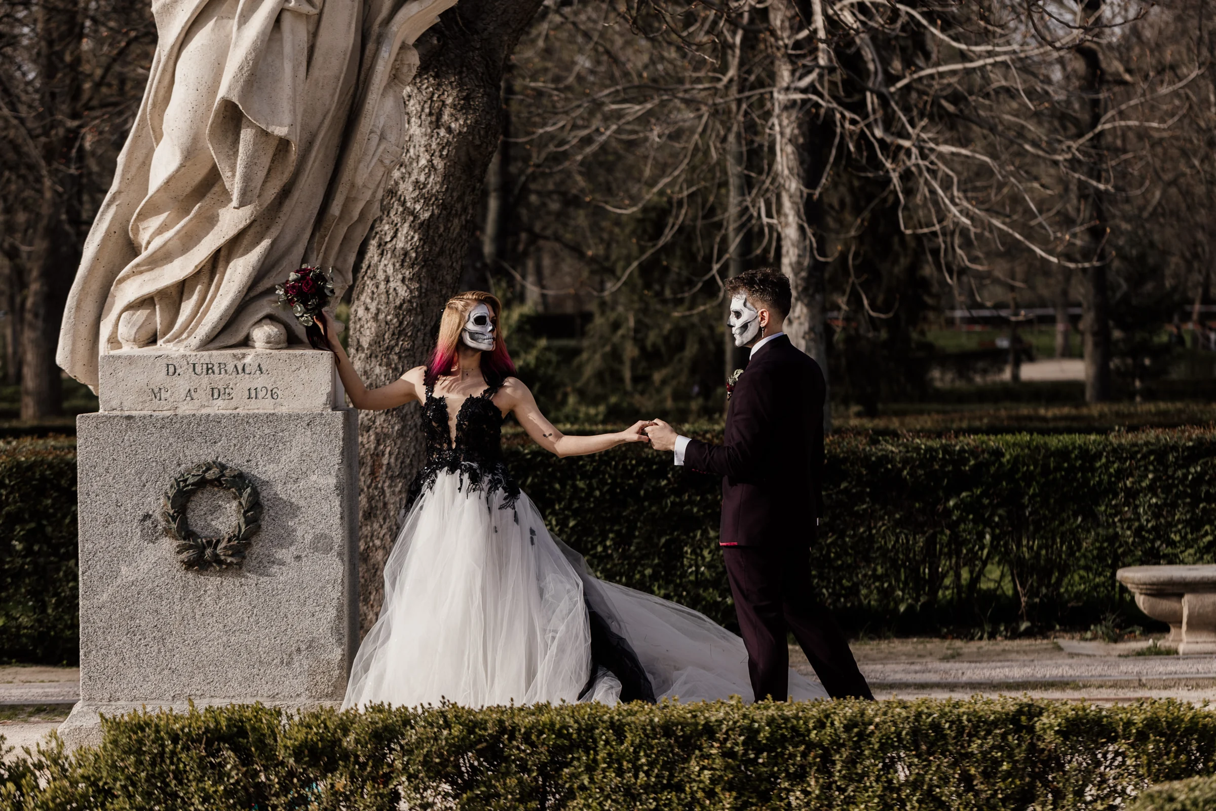 Silvia y Rubén se toman de la mano junto a la estatua de Doña Urraca en El Retiro durante su postboda gótica en Madrid.