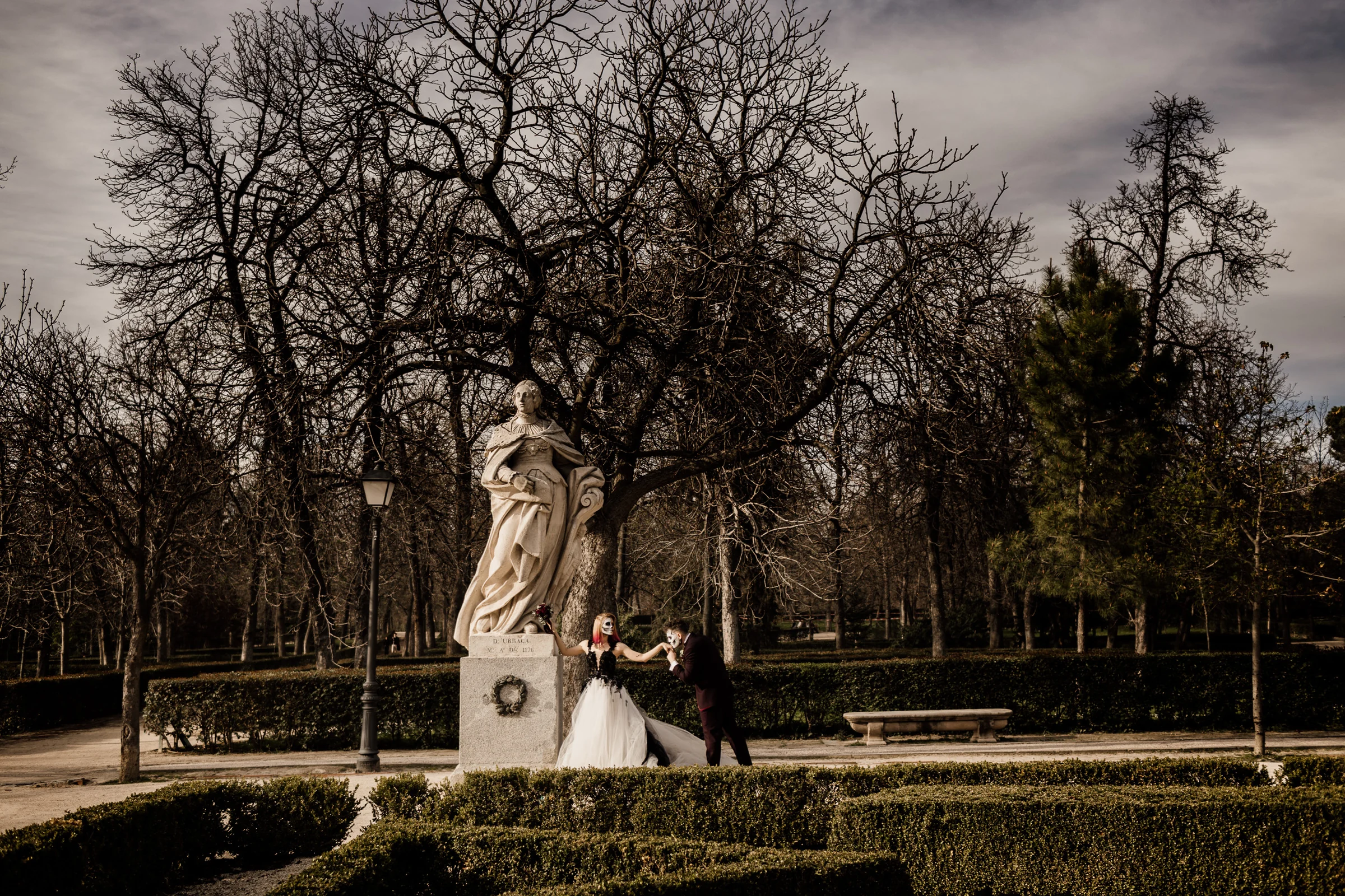 Silvia y Rubén posan junto a una estatua clásica rodeados por los jardines y árboles de El Retiro en un plano general.