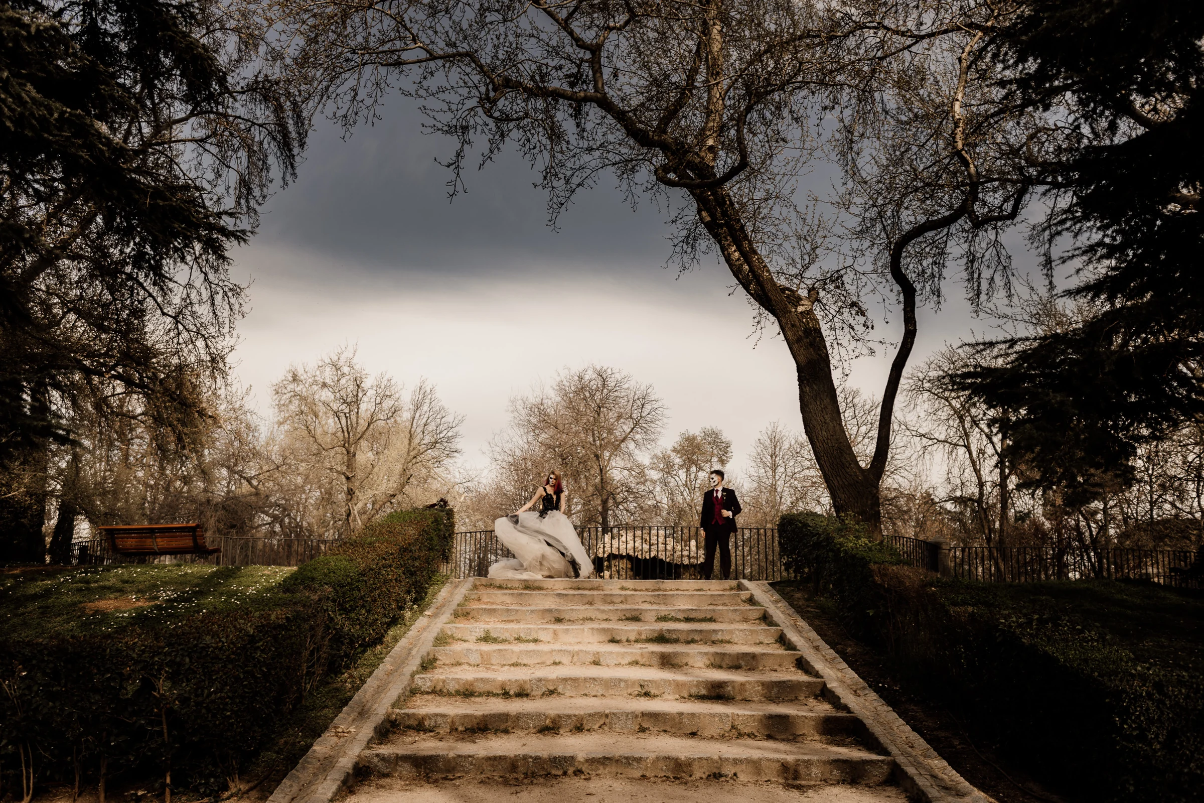 Silvia y Rubén aparecen separados en la parte alta de una escalinata de El Retiro bajo grandes árboles durante su postboda.