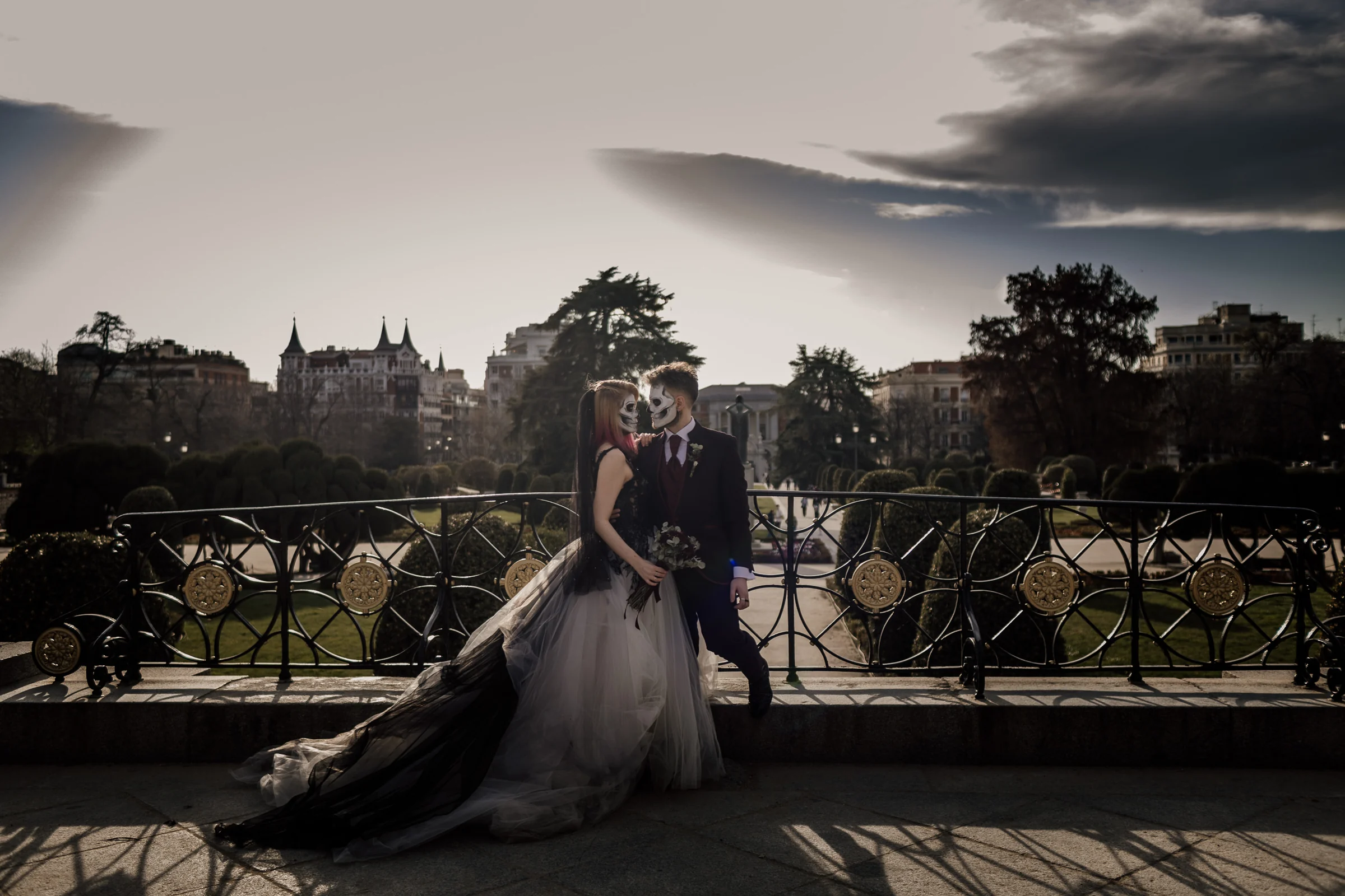 Silvia y Rubén posan junto a una barandilla de El Retiro con los jardines y edificios de Madrid al fondo en su postboda gótica.