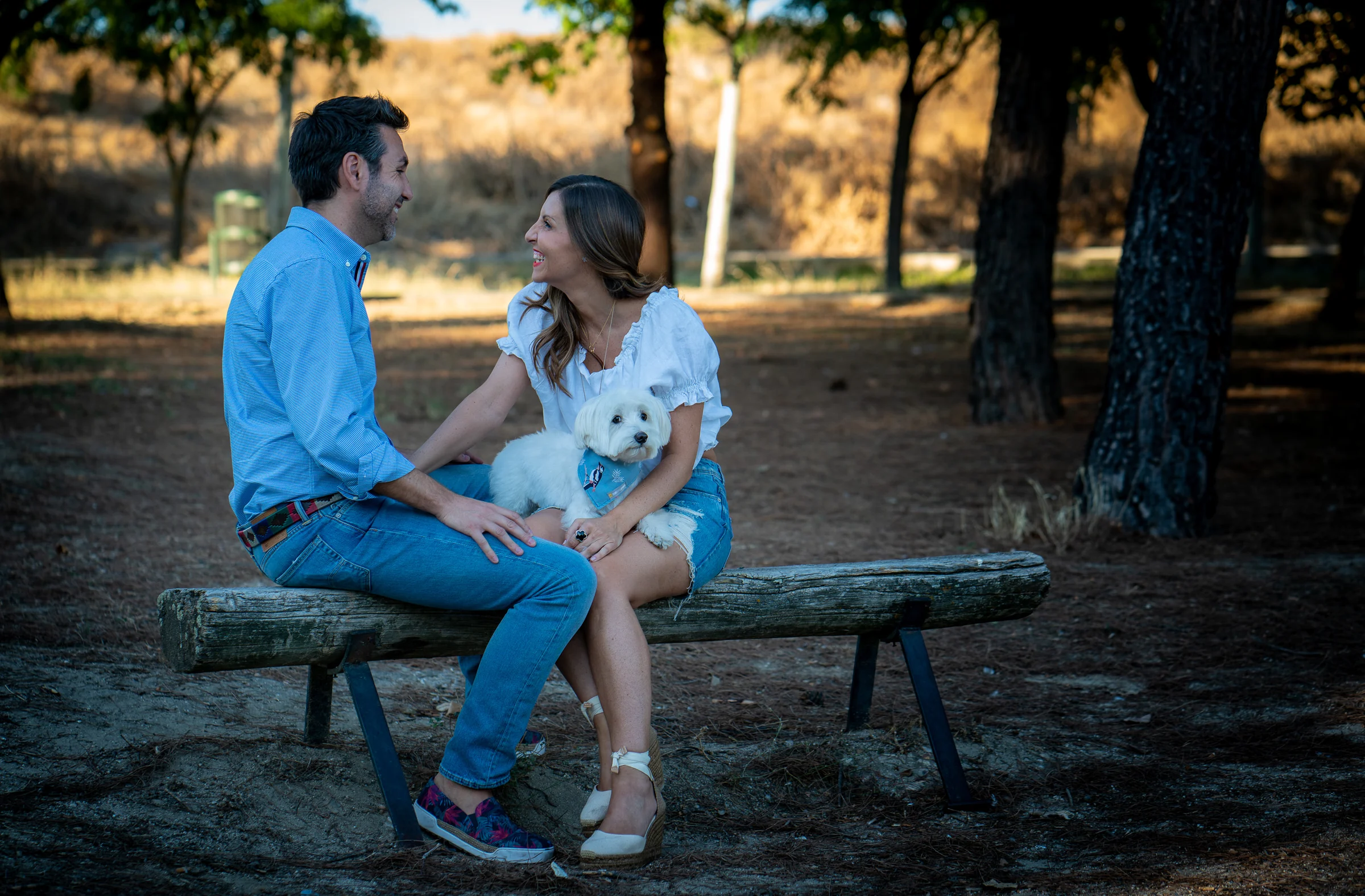 Vanesa y Fran conversan sentados en un banco de madera junto a su perro durante su preboda en un parque de Madrid.