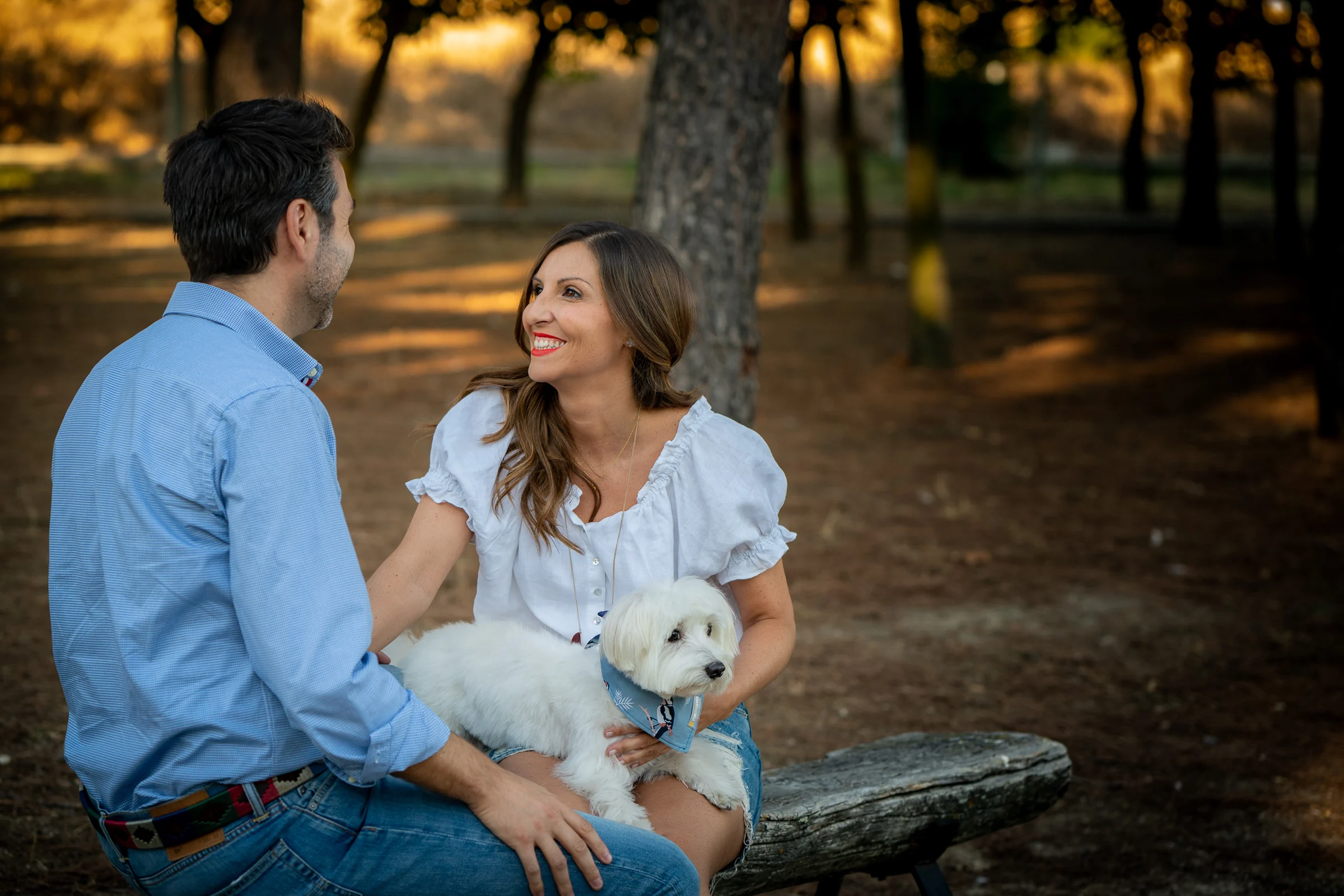 Vanesa y Fran se miran sonrientes sentados en un banco del parque durante su sesión de preboda en Madrid.