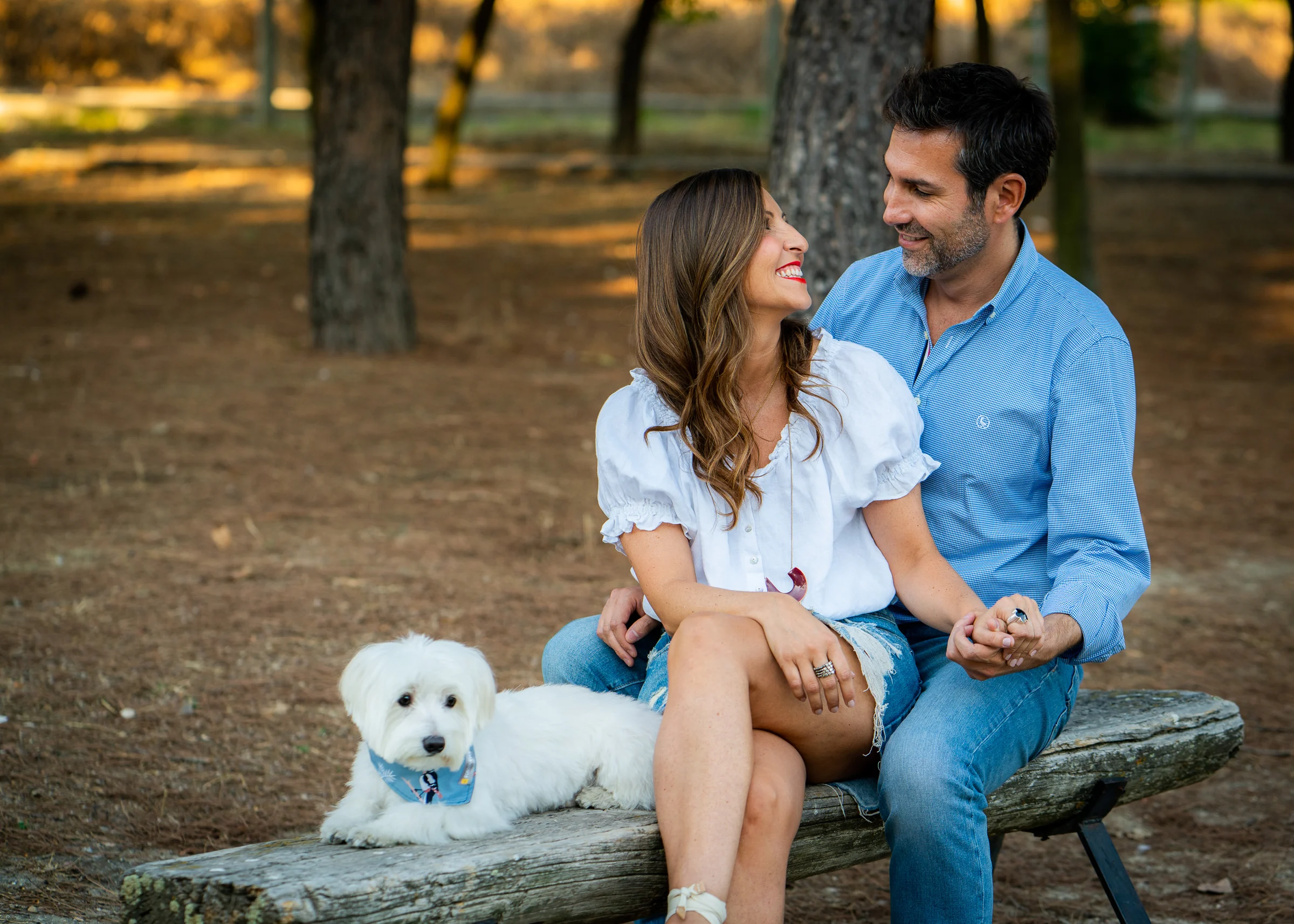 Vanesa y Fran posan sonrientes sentados en un banco del parque con su perro durante una tarde de preboda en Madrid.