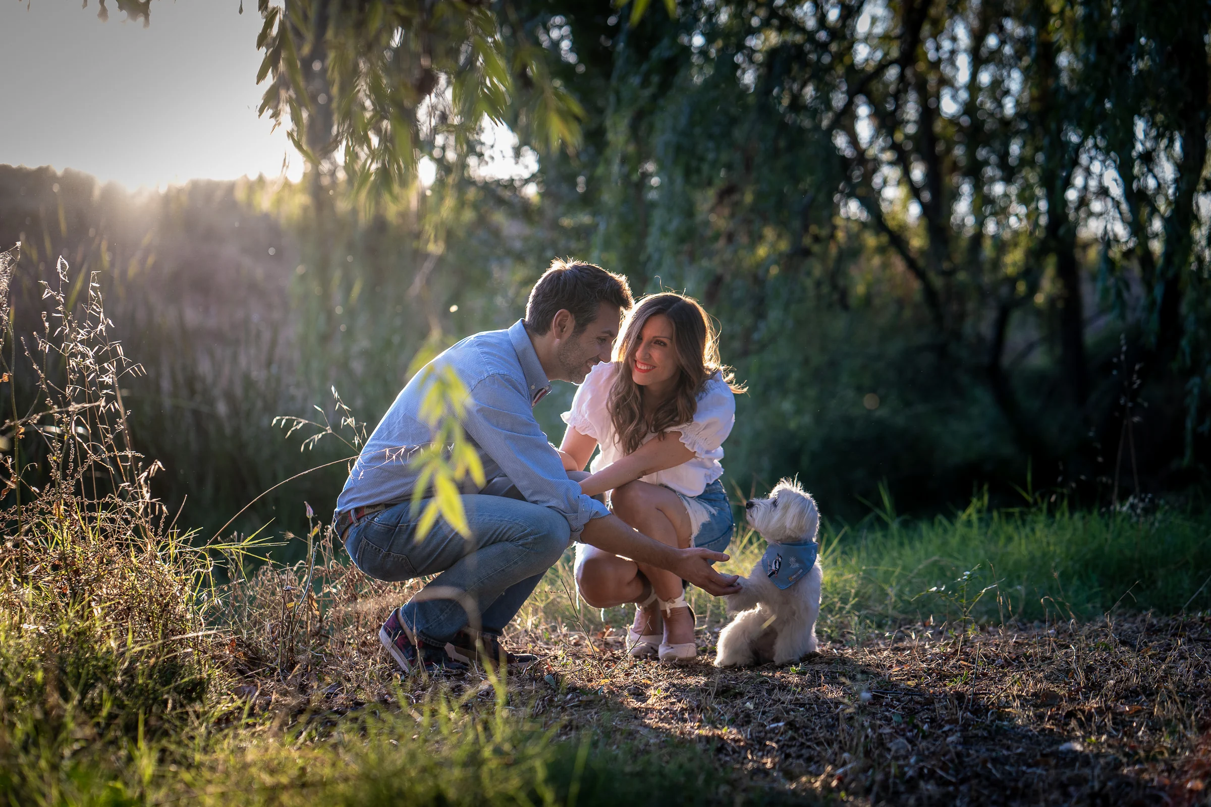 Vanesa y Fran se agachan junto a su perro en una zona de césped durante su preboda en Madrid.