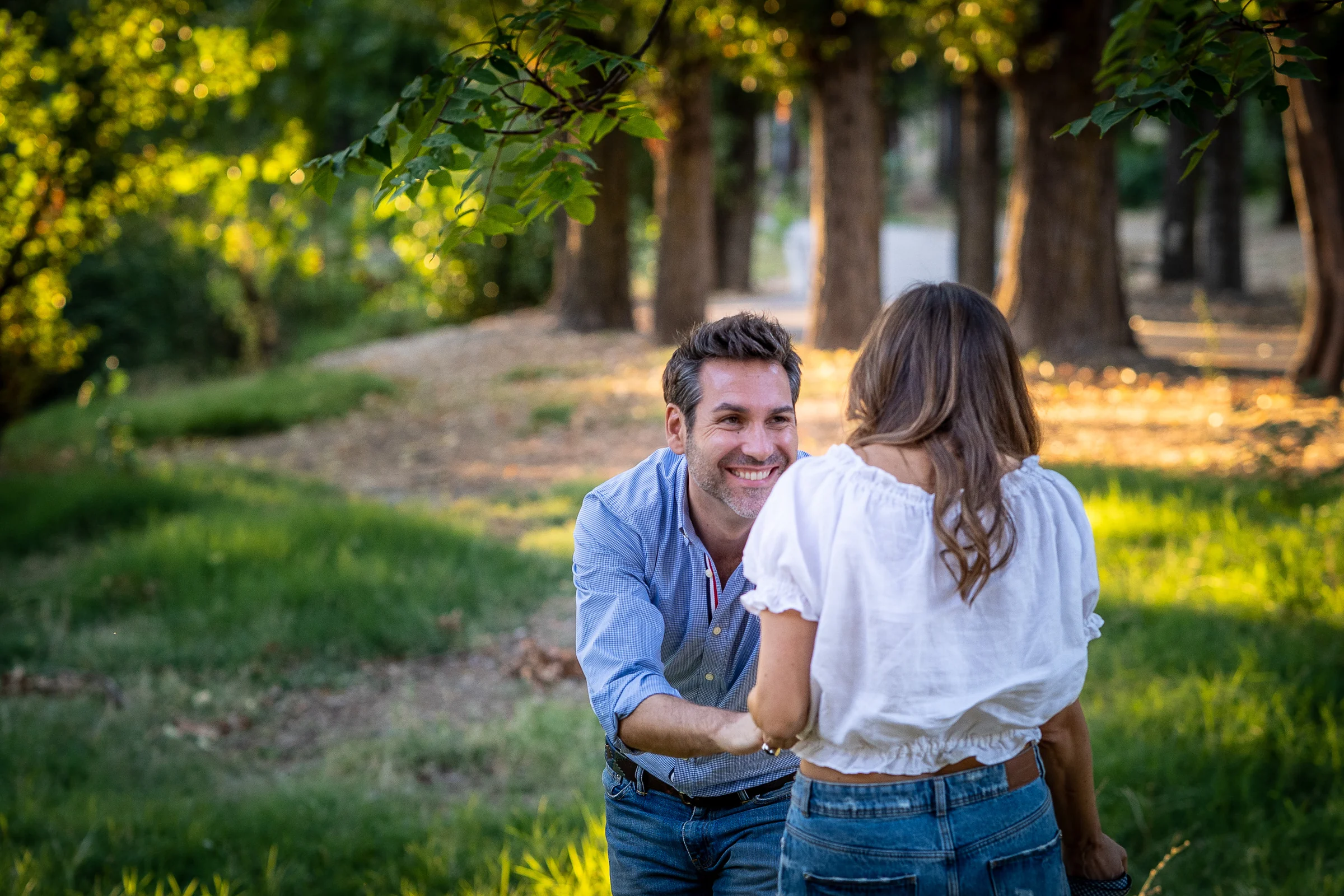 Fran se arrodilla frente a Vanesa en una pradera del parque durante su preboda en Madrid.