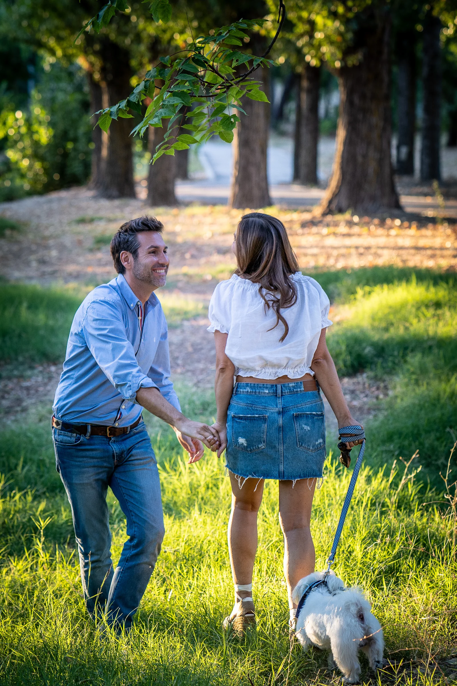 Vanesa y Fran se dan la mano mientras pasean por la pradera del parque en su preboda en Madrid.