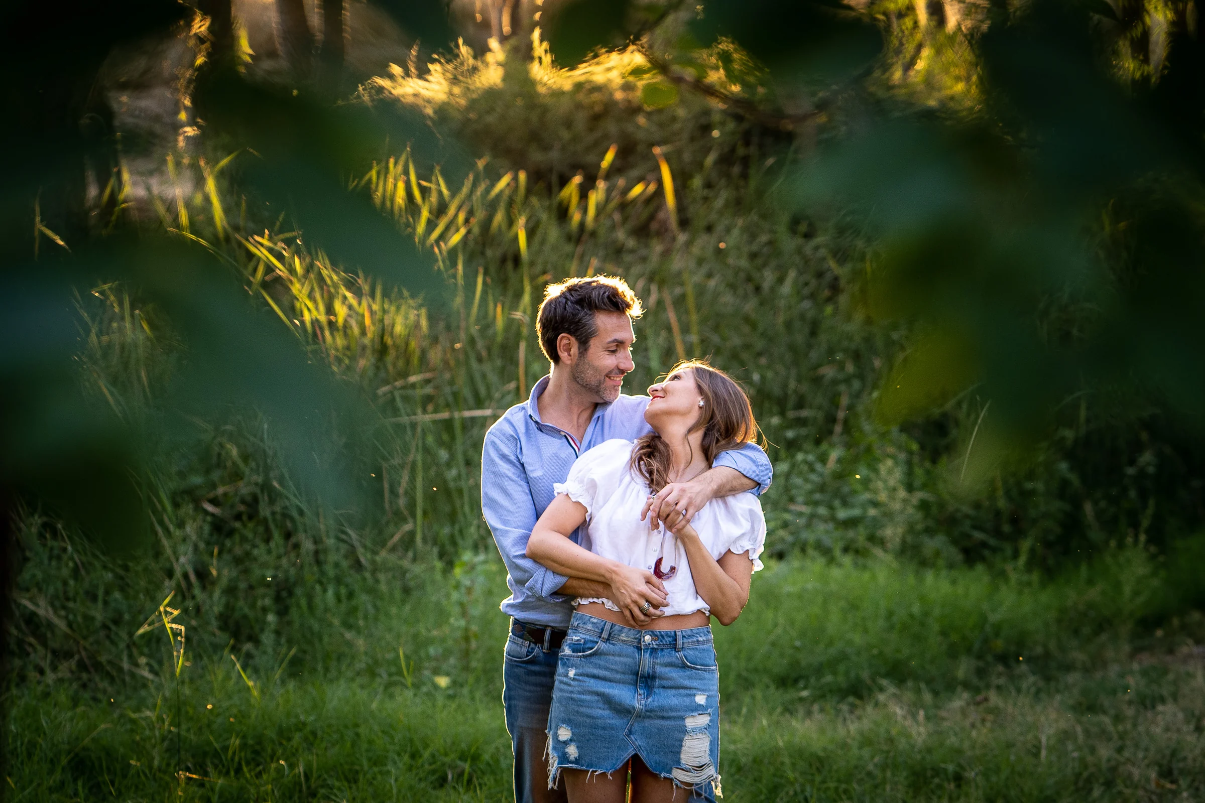 Vanesa y Fran se abrazan entre vegetación iluminada por la luz dorada en su preboda en Madrid.