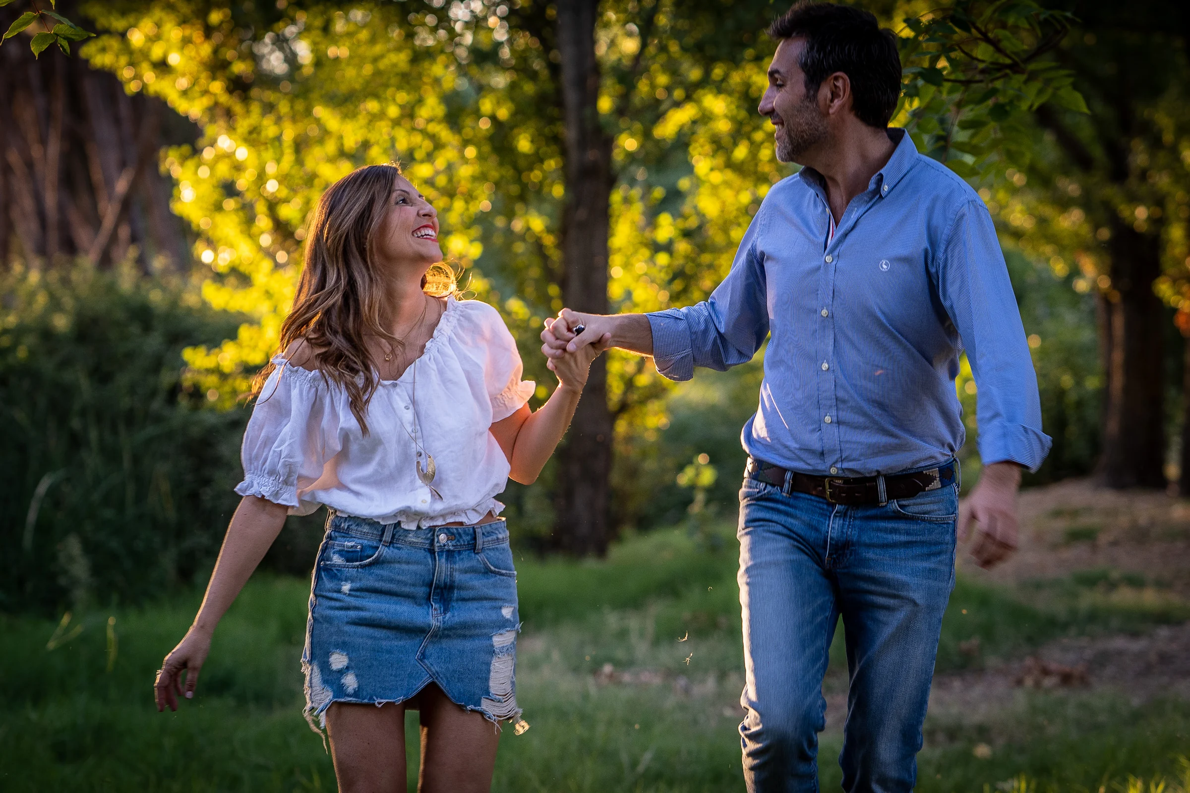 Vanesa y Fran pasean sonrientes entre árboles durante su preboda en un parque de Madrid.