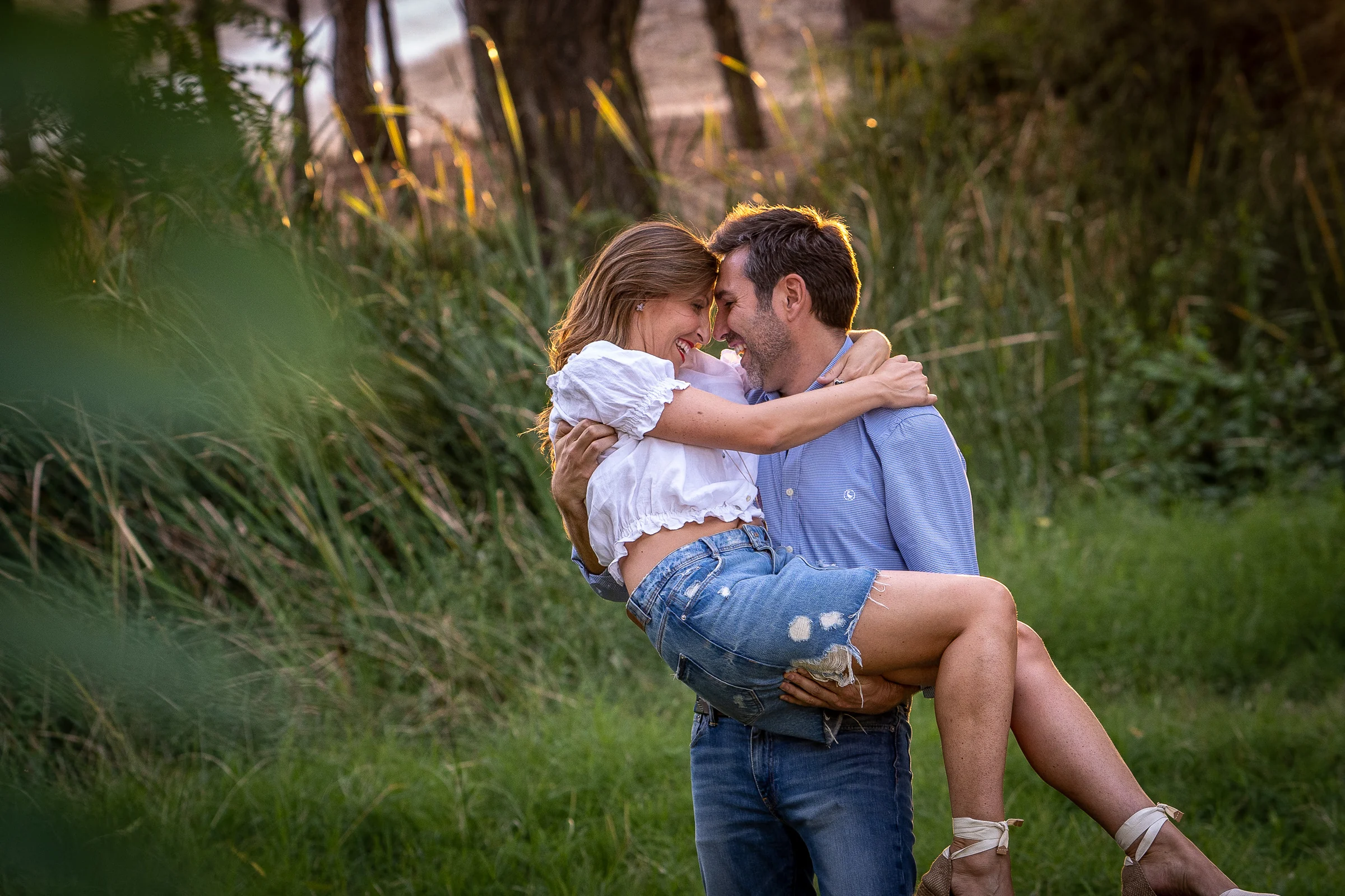 Vanesa y Fran se besan mientras Fran la sostiene en brazos durante su preboda en un parque de Madrid.